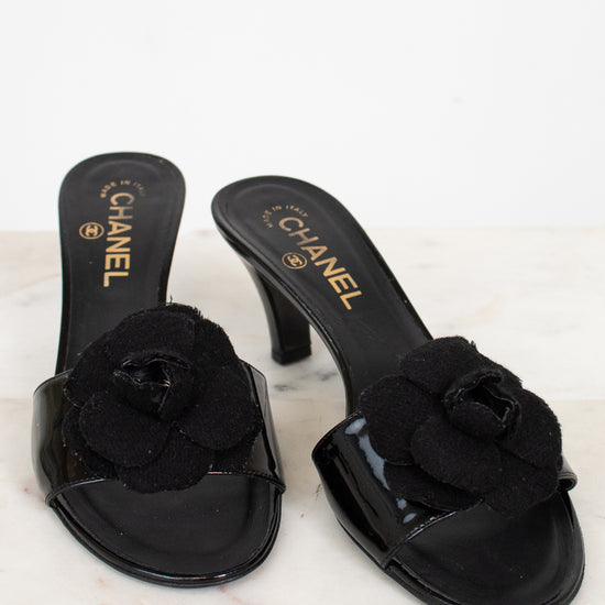 Black Chanel kitten heels with floral details on a marble surface