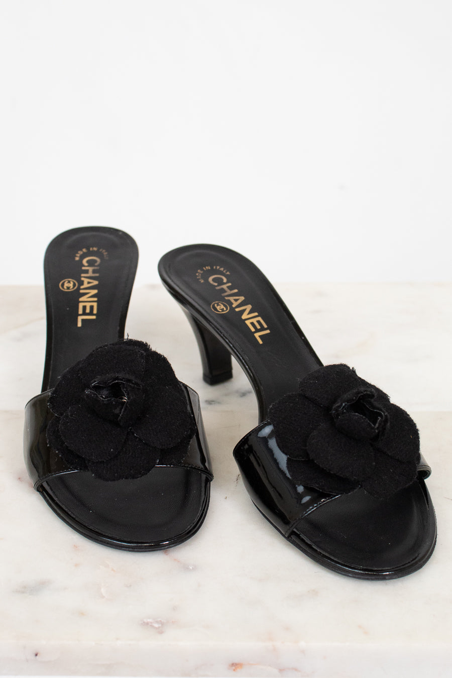 Black Chanel kitten heels with floral details on a marble surface