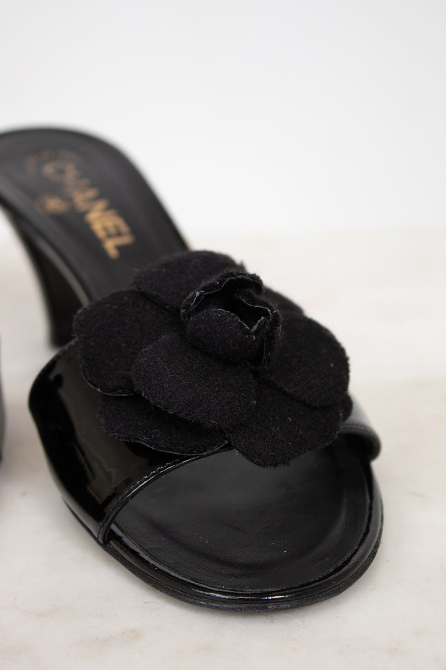 Black Chanel kitten heels with flower detail on a white background