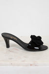Black Chanel kitten heel with a flower detail on a white marble surface