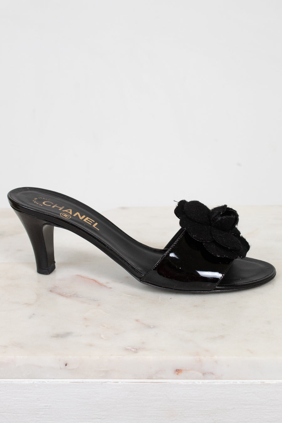 Black Chanel kitten heel with a flower detail on a white marble surface