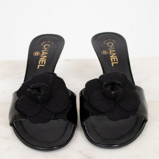 Black Chanel kitten heels with flower details on a white marble surface