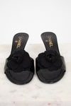 Black Chanel kitten heels with flower details on a white marble surface
