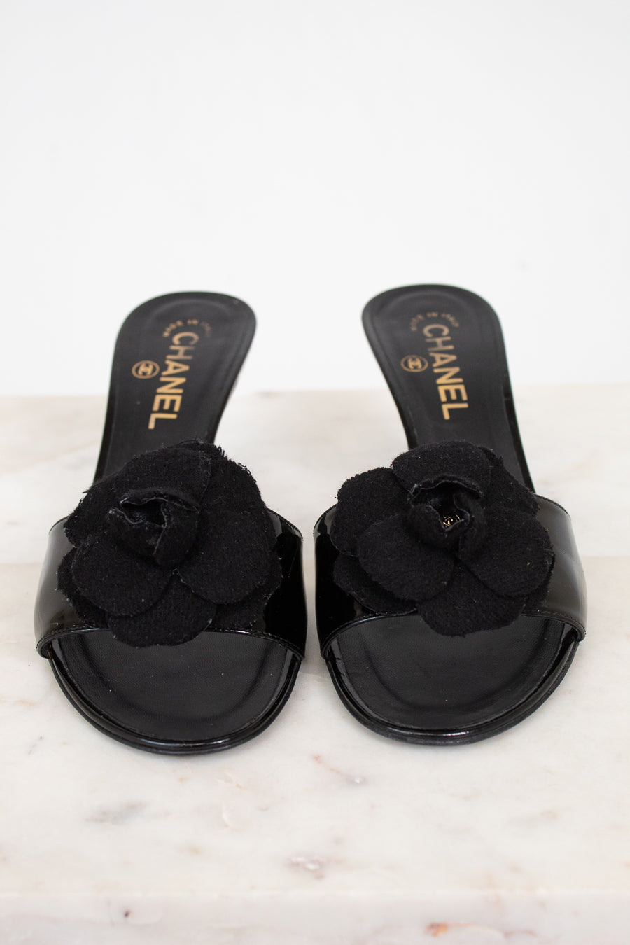 Black Chanel kitten heels with flower details on a white marble surface