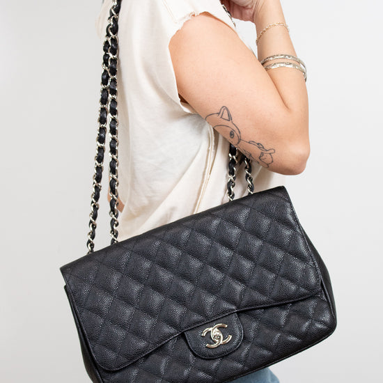 Person holding a black quilted handbag with a visible brand logo against a plain background