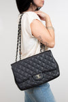 Person holding a black quilted handbag with a visible brand logo against a plain background