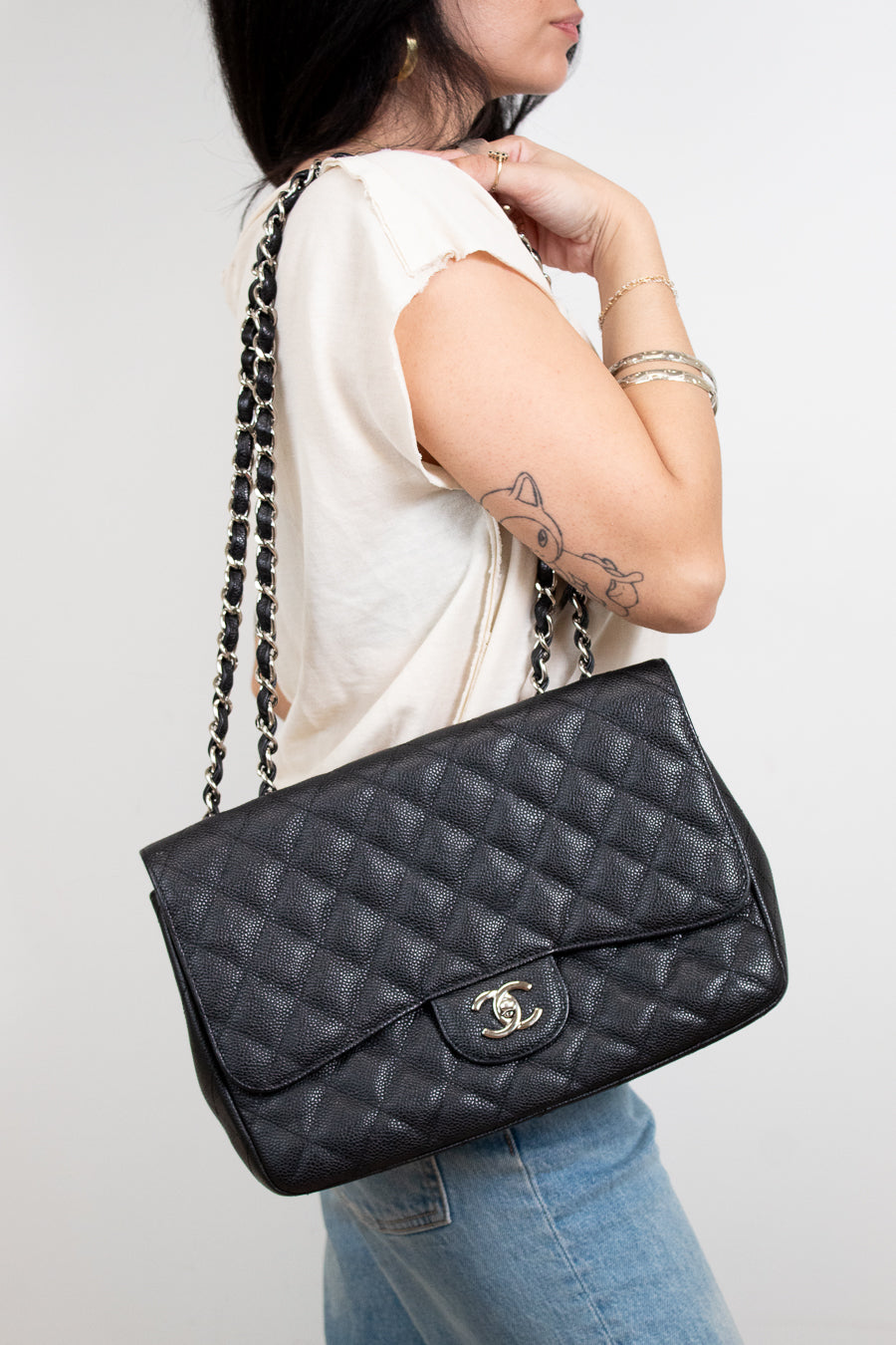 Person holding a black quilted handbag with a visible brand logo against a plain background