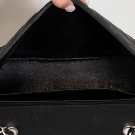 Close-up of a black handbag with a hand opening it, on a neutral background.