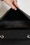 Close-up of a black handbag with a hand opening it, on a neutral background.