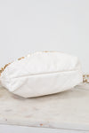 A white quilted leather shoulder bag with a gold chain strap, resting on a light marble surface against a white background.