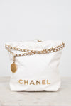 A white quilted leather Chanel bucket bag with gold-tone chain detailing and a gold CHANEL logo on the front, set against a light gray background.