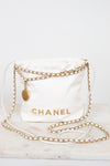 A white quilted Chanel shoulder bag with gold-tone chain straps and a gold CHANEL logo, displayed on a light marble surface against a white background.