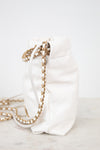 A white quilted leather bucket bag with a gold chain strap, resting on a light marble surface against a white background.