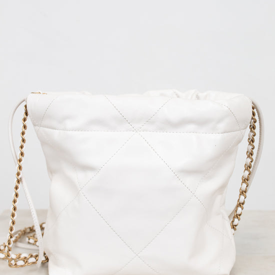 A white quilted leather shoulder bag with a gold chain strap, resting on a light marble surface against a white background.