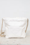 A white quilted leather shoulder bag with a gold chain strap, resting on a light marble surface against a white background.