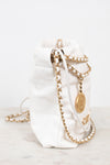 A white quilted leather bucket bag with gold-tone chain straps and a gold-tone CC logo medallion, resting on a light marble surface against a white background.
