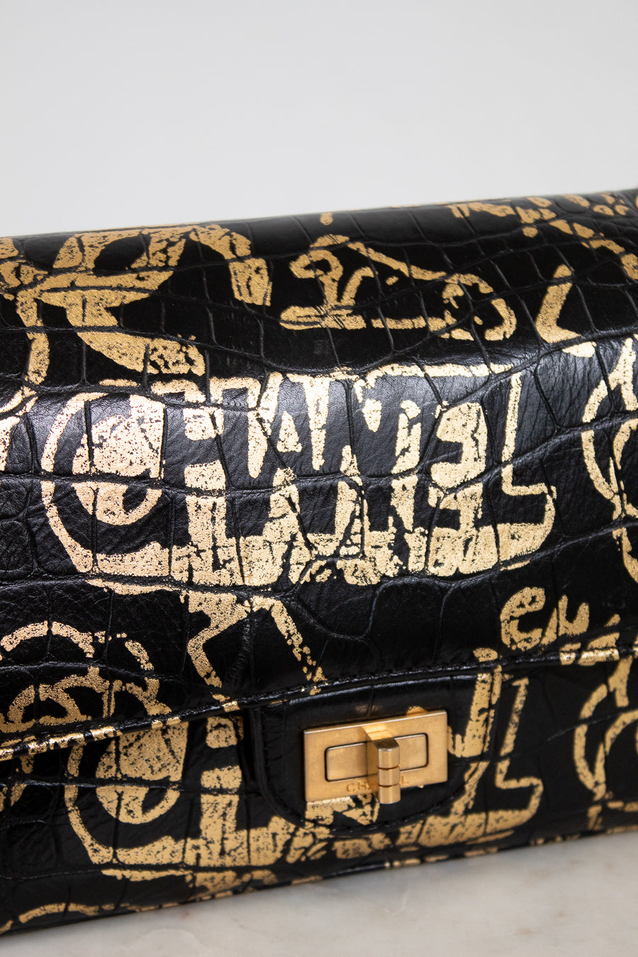 Black handbag with gold logo pattern on a light gray background