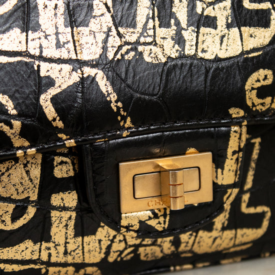 Black and gold patterned handbag with a gold clasp on a light gray background