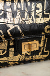 Black and gold patterned handbag with a gold clasp on a light gray background