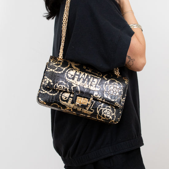 Person wearing a black outfit with a Chanel handbag on a plain background