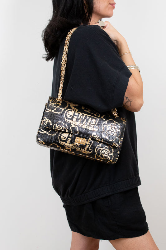 Person wearing a black outfit with a Chanel handbag on a plain background