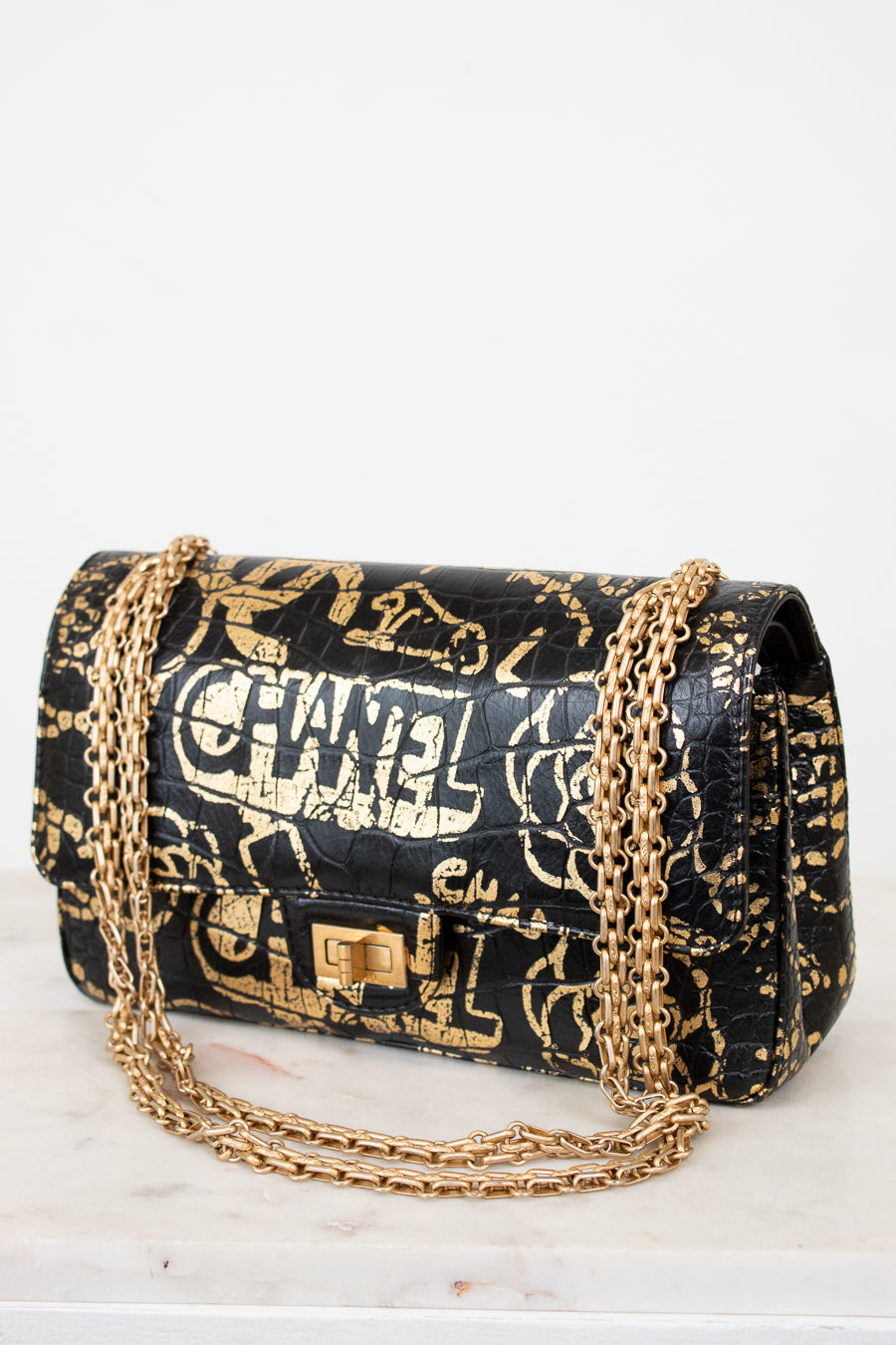 Black handbag with gold chain strap and graffiti-style text on a white background