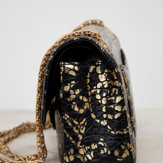 Black handbag with gold chain strap on a marble surface