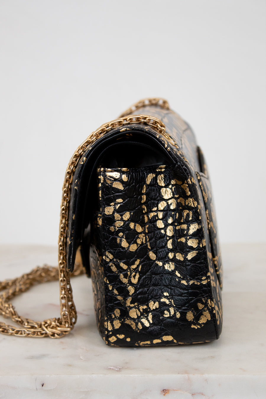 Black handbag with gold chain strap on a marble surface