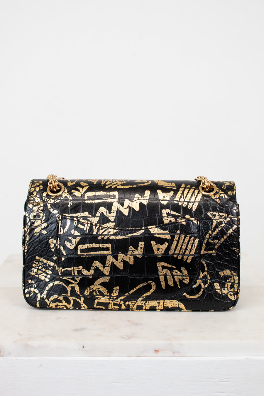 Black handbag with gold geometric pattern on a white background