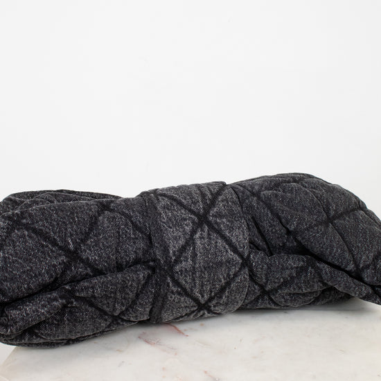 A dark gray quilted denim-like handbag with a quilted stitched pattern, resting on a white marble surface against a white background.