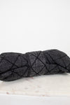 A dark gray quilted denim-like handbag with a quilted stitched pattern, resting on a white marble surface against a white background.