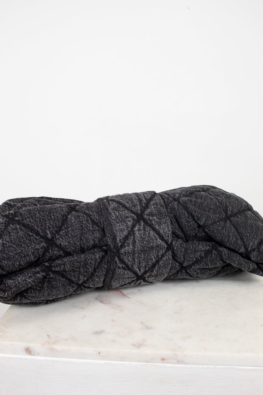 A dark gray quilted denim-like handbag with a quilted stitched pattern, resting on a white marble surface against a white background.