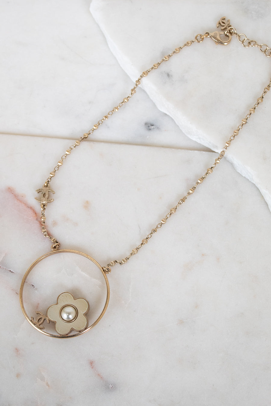 Gold necklace with a floral pendant on a marble surface