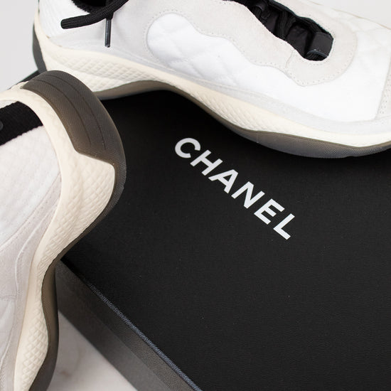 White and black Chanel sneakers on a black box with 'Chanel' branding.