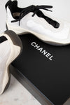 White and black Chanel sneakers on a black box with 'Chanel' branding.