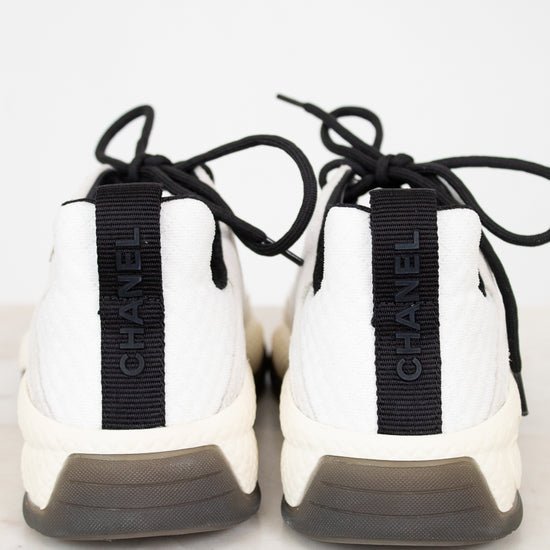 White sneakers with black laces and 'Chanel' branding on a light background