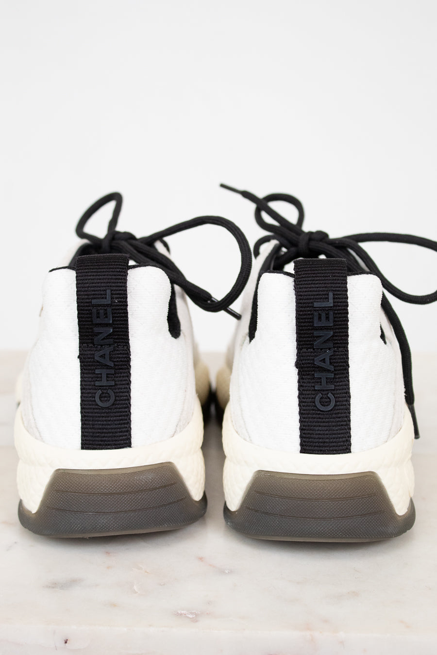 White sneakers with black laces and 'Chanel' branding on a light background