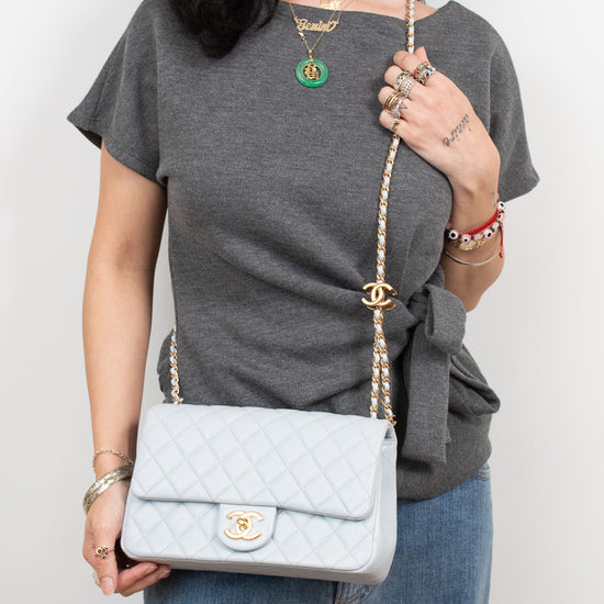 A woman wearing a gray t-shirt and blue jeans carries a light blue quilted Chanel shoulder bag with a gold chain strap and CC turn-lock closure.