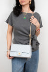 A woman wearing a gray t-shirt and blue jeans carries a light blue quilted Chanel shoulder bag with a gold chain strap and CC turn-lock closure.