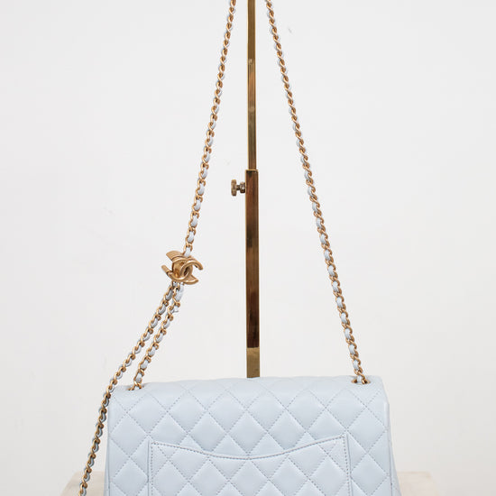 A light blue quilted leather shoulder bag with gold-tone chain straps and a gold interlocking CC logo charm, displayed on a stand against a white background.