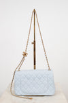 A light blue quilted leather shoulder bag with gold-tone chain straps and a gold interlocking CC logo charm, displayed on a stand against a white background.