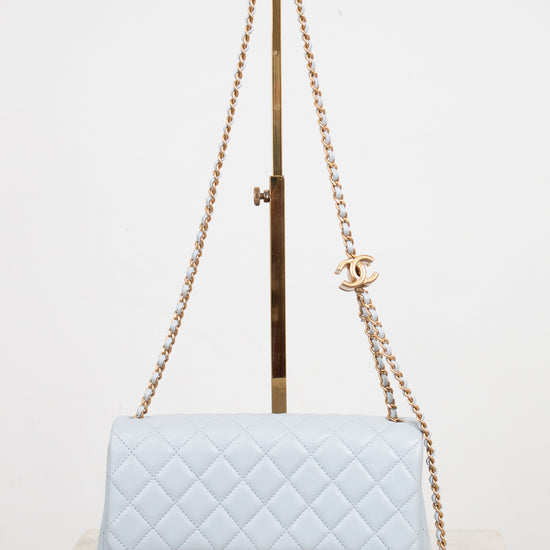 A light blue quilted leather shoulder bag with gold-tone hardware, displayed on a stand against a plain white background.