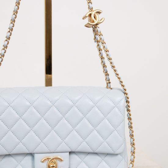 A light blue quilted Chanel flap bag with gold-tone hardware, shown on a display stand against a clean white background.