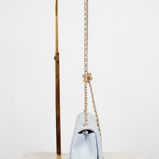 A light blue quilted leather shoulder bag with a gold chain strap, displayed on a gold metal stand against a white background.