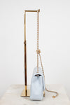 A light blue quilted leather shoulder bag with a gold chain strap, displayed on a gold metal stand against a white background.