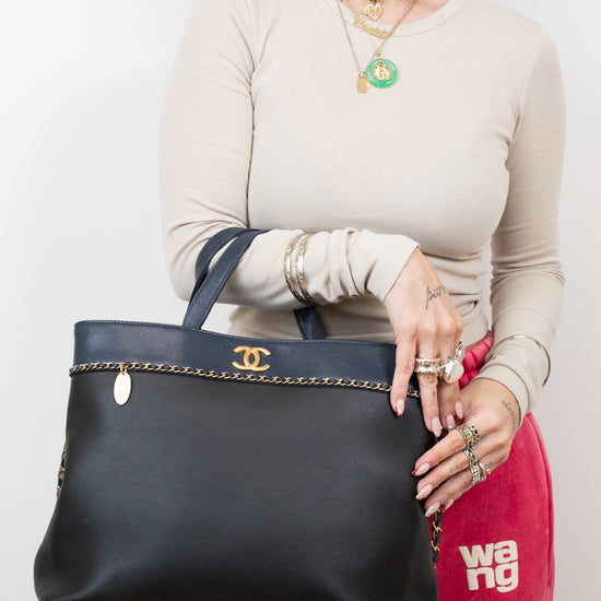 Person holding a black handbag with a visible brand logo against a plain background