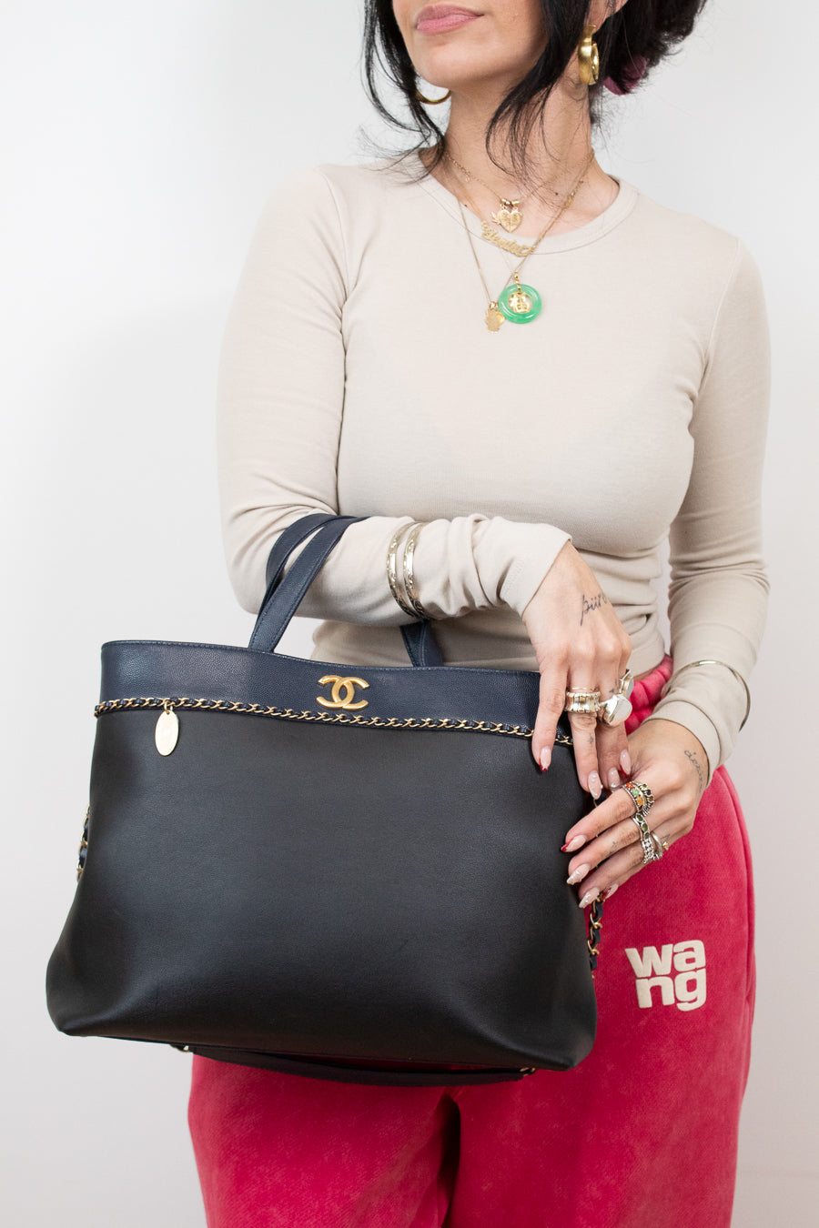 Person holding a black handbag with a visible brand logo against a plain background