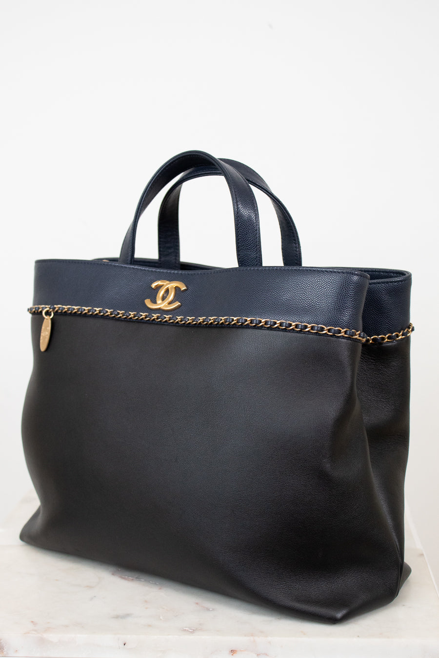 Black handbag with gold chain detail and logo on a white background