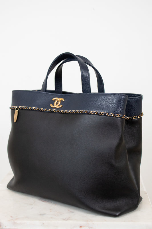 Black handbag with gold chain detail and logo on a white background