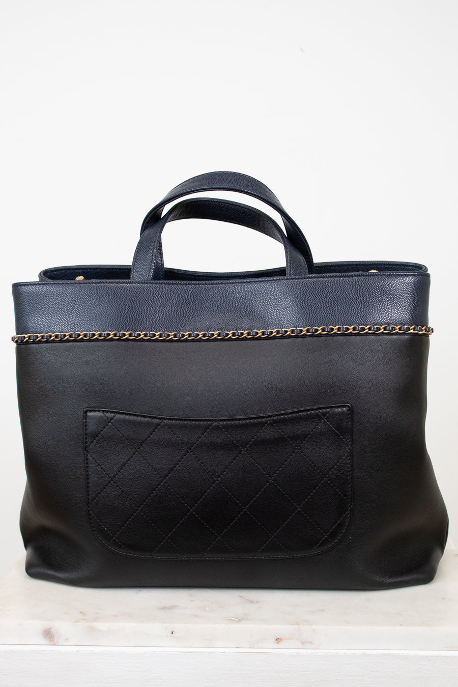 Black leather tote bag with chain detail on a white background